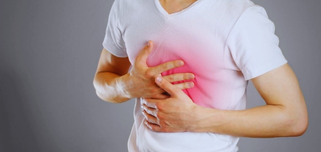 أسباب الحموضة المعوية (Heartburn)؛ رجل يرتدي كنزة بيضاء يضع يديه على صدره من حرقة المعدة.