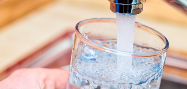 ماذا ينتج عن نقص الماء في الجسم؛ كأس زجاجي يصب فيه صنبور ماء.