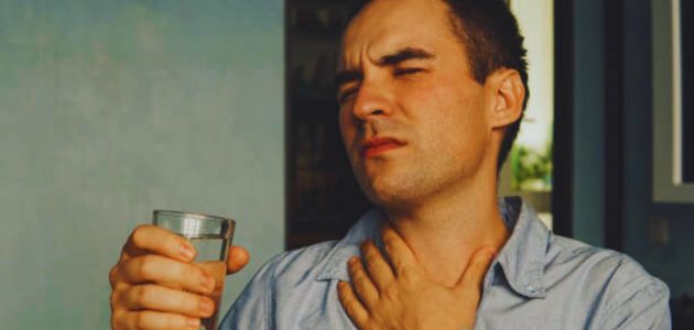 هل جفاف الحلق من اعراض كورونا؛ رجل يمسك كأس ماء ويضع يده الأخرى على عنقه.